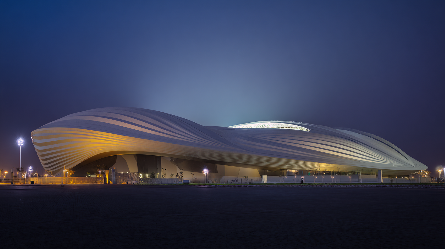 Render of Al Janoub Stadium in Al Wakrah, Qatar designed by Zaha Hadid, showing sweeping sail-shaped rooflines inspired by Qatari dhows, illuminated against a twilight sky, photographed from a wide low-angle to emphasize curvature and monumental scale.