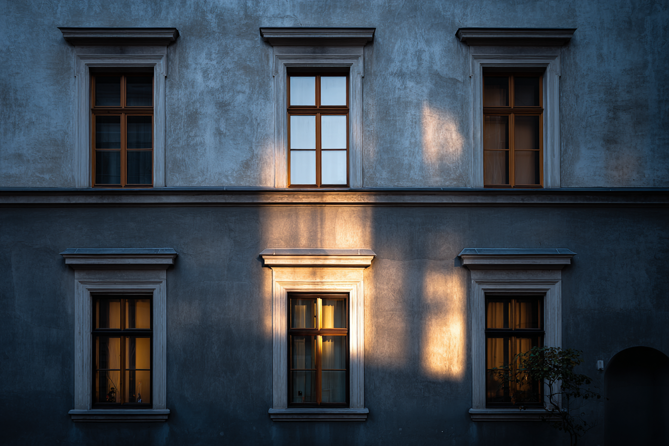 Viennese townhouse façade with cool blue-gray plaster and wooden window frames, illuminated by soft evening light, expressing quiet architectural restraint.