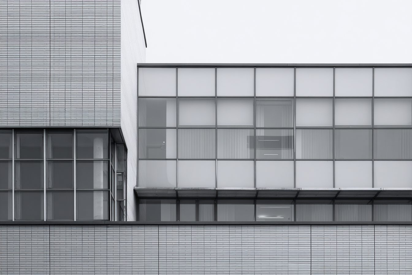 Modernist building with gridded glass panels and concrete surfaces, captured in soft light with calm tone and refined minimalist realism.