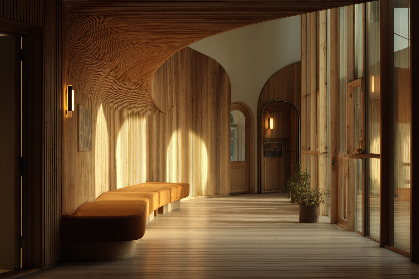 Curved wooden corridor of Paimio Sanatorium illuminated by warm morning light, soft shadows across benches and glass panels, expressing Alvar Aalto’s organic modernist design.